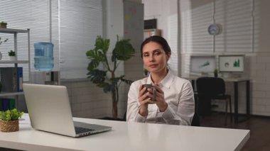 İş hayatı konsepti. İş kadını ofiste masa başında yemek dağıtımı yapıyor, sandalyeye oturup kahve içiyor, taze aromatik içeceklerin tadını çıkarıyor. Yavaş çekim