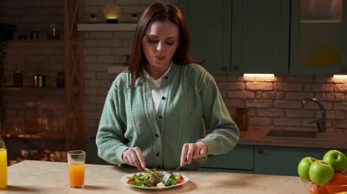 Sağlıklı beslenme konsepti. Mutfaktaki masada akşam yemeği için sağlıklı sebze salatası hazırlayan kadın taze salata yiyen, portakal suyu içen ve tadını çıkartan kadın. Yavaş çekim