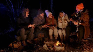 Bir grup genç arkadaş gece bir kamp ateşinin etrafında toplanmış, bir tanesi gitar çalarken müziğin keyfini çıkarıyorlardı. Sıcak kış kıyafetleri giymişler, birlikte gülüyorlar ve şarkı söylüyorlar..