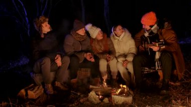 Bir grup genç arkadaş gece bir kamp ateşinin etrafında toplanmış, bir tanesi gitar çalarken müziğin keyfini çıkarıyorlardı. Sıcak kış kıyafetleri giymişler, birlikte gülüyorlar ve şarkı söylüyorlar..