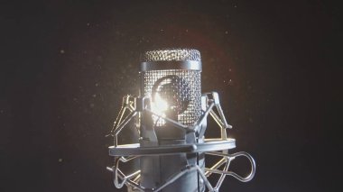 Dramatik arka ışıklandırma ve yüzen toz parçacıkları ile profesyonel bir yoğunlaştırıcı mikrofonun yakın çekimi, sanatsal ve atmosferik bir stüdyo sahnesi yaratıyor..