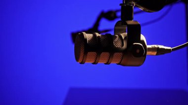 Ses çıkaran bir kolun üzerine yerleştirilmiş yüksek kaliteli bir mikrofon. Mavi ışıklı bir stüdyonun arka planına kurulmuş. Podcast, yayın ve profesyonel ses kaydı için ideal.