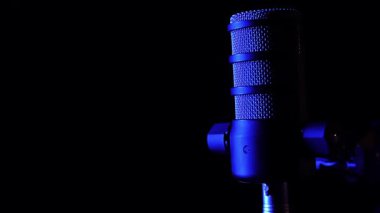 Profesyonel bir mikrofon. Siyah arka planda sarı ve mavi ışıkla aydınlatılıyor. Müzik, podcast ve yayın için minimalist ve fütürist bir kavram.