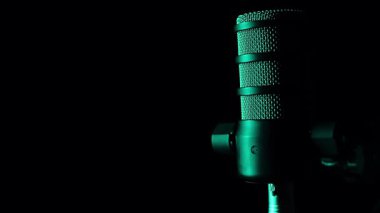 Profesyonel bir mikrofon. Siyah arka planda sarı ve mavi ışıkla aydınlatılıyor. Müzik, podcast ve yayın için minimalist ve fütürist bir kavram.