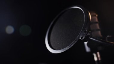 Yumuşak, sıcak ışıklandırmayla aydınlatılmış, pop filtresi olan yüksek kaliteli bir stüdyo mikrofonu. Bir stüdyo ortamında podcast, seslendirme ve profesyonel ses kaydı için ideal.