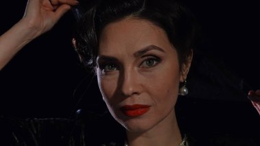 Stüdyoda profesyonel model. Siyah arka planda izole edilmiş, eski moda saç stili ve makyajlı kadın oyuncu. Yüzünden peçesini çıkarırken çekilmiş yakın plan..