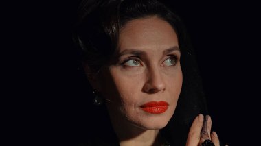 Stüdyoda profesyonel model. Siyah arka planda izole edilmiş, eski moda saç stili ve makyajlı kadın oyuncu. Yüzünden peçesini çıkarırken çekilmiş yakın plan..