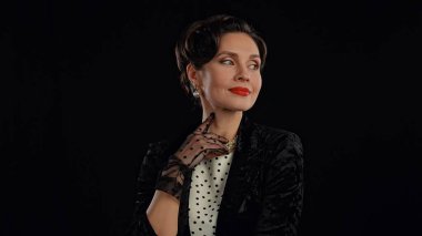 Stüdyoda profesyonel model. Siyah arka planda izole edilmiş, eski moda saç stili ve makyajlı kadın oyuncu, gülümseyen ve başka tarafa bakan kadın..