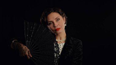 Stüdyoda profesyonel model. Siyah arka planda izole edilmiş, eski moda saç stili ve makyajlı kadın oyuncu, dantel pervaneli poz veren kadın..