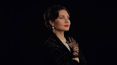 Stüdyoda profesyonel model. Siyah arka planda izole edilmiş, eski moda saç stili ve makyajlı kadın oyuncu, gülümseyen ve başka tarafa bakan kadın..