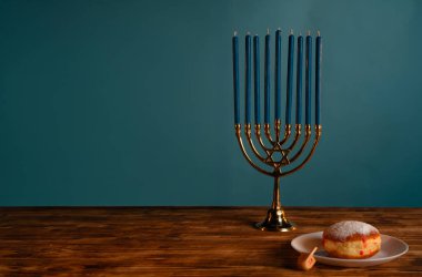 Geleneksel bir dreidel ve çöreğin yanında mavi mumları olan bir Hanuka menorası, ışık festivalini simgeliyor..
