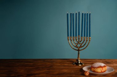 Klasik bir Hanukkah sahnesi. Menorah, dreidel ve sufganiyah ahşap bir masada, şenlikli ruhu sembolize ediyor..