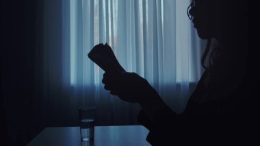 Loş bir odada para sayan bir kişinin silüeti. Yakınlardaki masanın üzerine bir bardak su konur..