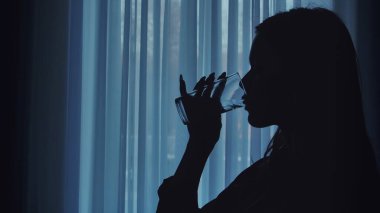 Bir bardaktan su içen bir insanın silüeti yumuşak, aydınlık bir perde arkasında..