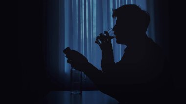 Arka planda penceresi olan akıllı telefonu tutarken bardaktan su içen bir kişinin silüeti..