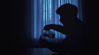 Mavi perdeli loş bir odada bardağa su döken bir insanın silueti huzurlu bir ortam yaratıyor..