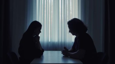 Bu resim, iki insanın bir pencereye karşı oturup yüz yüze oturarak derin bir konuşma ve bağlantı hissi yarattığını gösteriyor..