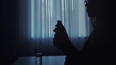 Loş bir odada para sayan bir kişinin silüeti. Yakınlardaki masanın üzerine bir bardak su konur..