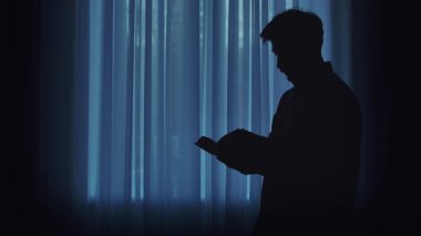 Pencerenin kenarında kitap okuyan, barışçıl ve iç gözlemci bir atmosfer yaratan bir kişinin silüeti..