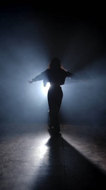 Modern koreografi yaratıcı konsept. Stüdyoda dans eden bir kadının silueti. Siyah arka plan dumanla dolu, beyaz ışıklar arkadan parlıyor..