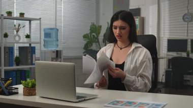 Yaratıcı iş konsepti. Genç işletmeci kadın yönetici büroda oturmuş kağıtlarla çalışıyor. Dizüstü bilgisayar kullanıyor, hayal kırıklığına uğramış ifade kağıtları atıyor, ayağa kalkıyor ve dans ediyor ve gülümsüyor..