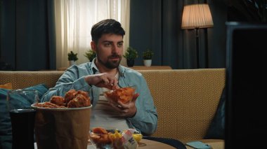 Abur cubur reklamı konsepti. Sakallı adam evde fast food dağıtımı ile vakit geçiriyor, kanepede oturuyor televizyon izliyor ve patates cipsi yiyor..