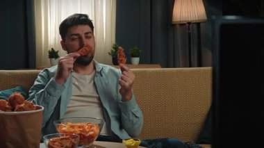 Abur cubur reklamı konsepti. Sakallı adam evde fast food teslimatlarıyla vakit geçiriyor, kanepede oturup televizyon seyrediyor, arkadaşının tavuğunu elinde tutuyor, kokluyor ve ısırıyor, tadını çıkarıyor. Yavaş çekim