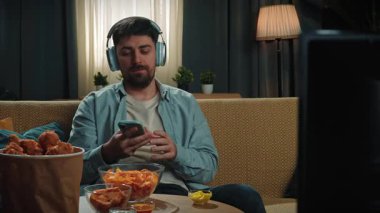 Abur cubur reklamı konsepti. Sakallı adam evde fast food dağıtımı ile vakit geçiriyor, kanepeye oturuyor kulaklıkla müzik dinliyor ve kızarmış tavuk yiyor. Yavaş çekim