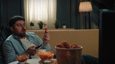 Abur cubur reklamı konsepti. Sakallı adam evde fast food dağıtımı ile vakit geçiriyor, kanepede uzanıyor, televizyon izliyor ve kızarmış tavuk yiyor. Yavaş çekim