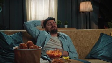 Abur cubur reklamı konsepti. Sakallı adam evde fast food dağıtımı ile vakit geçiriyor, kanepeye oturuyor ve televizyon seyrediyor, uykulu esniyor ve uykuya dalıyor. Yavaş çekim