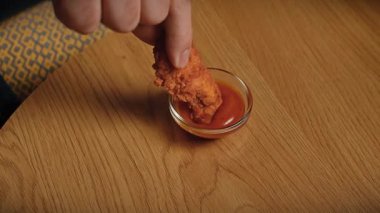 Abur cubur reklamı konsepti. Sakallı adamın yakın plan fotoğrafı, sosa batırılmış tavuk tutan ve çiğneyen, fast food yemekten hoşlanan adam. Yavaş çekim