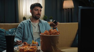 Abur cubur reklamı konsepti. Sakallı adam evde fast food dağıtımı yapıyor, kanepeye oturup televizyon izliyor, tavuk budu yiyor..