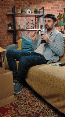 Abur cubur reklamı konsepti. Adam evde fast food dağıtımı ile vakit geçiriyor, kanepede oturup televizyon izliyor, sosa batırılmış tavuk yiyor, kola içiyor, tadını çıkarıyor..