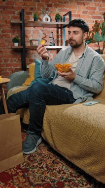 Abur cubur reklamı konsepti. Sakallı adam evde fast food dağıtımı ile vakit geçiriyor, kanepede oturuyor televizyon izliyor ve patates cipsi yiyor..