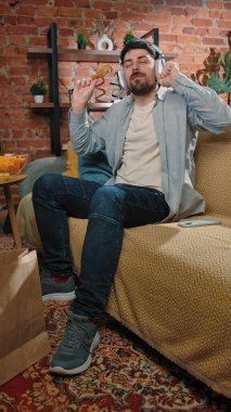 Abur cubur reklamı konsepti. Sakallı adam evde fast food dağıtımı ile vakit geçiriyor, kanepeye oturuyor kulaklıkla müzik dinliyor ve kızarmış tavuk yiyor..