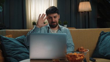 Abur cubur reklamı konsepti. Sakallı adam evde fast food dağıtımı ile vakit geçiriyor, kanepeye oturup bilgisayardan video görüşmesi yapıyor ve soslu kızarmış patates yiyor..