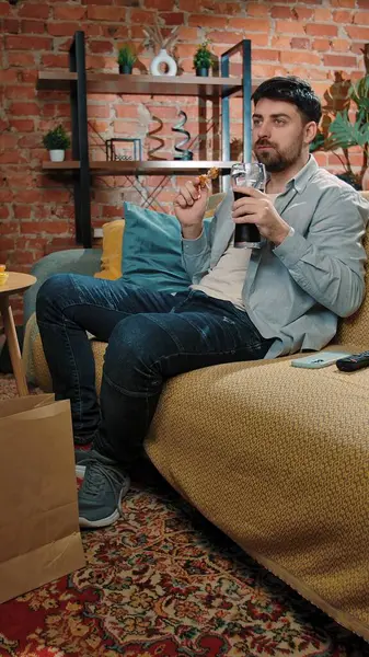 Abur cubur reklamı konsepti. Adam evde fast food dağıtımı ile vakit geçiriyor, kanepede oturup televizyon izliyor, sosa batırılmış tavuk yiyor, kola içiyor, tadını çıkarıyor..