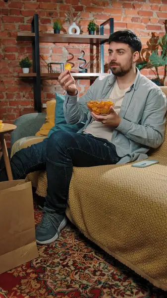 Abur cubur reklamı konsepti. Sakallı adam evde fast food dağıtımı ile vakit geçiriyor, kanepede oturuyor televizyon izliyor ve patates cipsi yiyor..