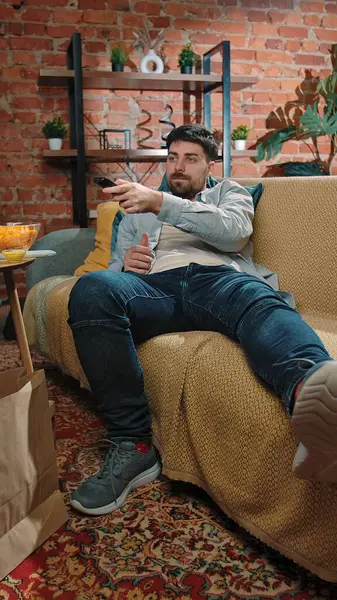 Abur cubur reklamı konsepti. Sakallı adam fast food dağıtımı ile evde vakit geçiriyor, kanepeye uzanıyor, televizyon seyrediyor..