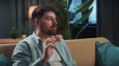 Abur cubur reklamı konsepti. Sakallı adam evde fast food dağıtımı ile vakit geçiriyor, kanepede oturuyor televizyon izliyor uzaktan kumandayla kanal değiştiriyor ve kızarmış tavuk bacağı yiyor..