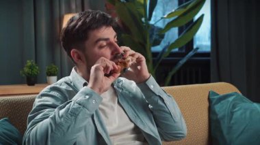 Abur cubur reklamı konsepti. Sakallı adam evde fast food dağıtımı ile vakit geçiriyor, kanepede oturuyor tavuk budu yiyor ve akıllı telefondan konuşuyor..