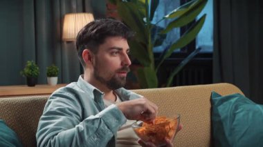 Abur cubur reklamı konsepti. Sakallı adam evde fast food dağıtımı ile vakit geçiriyor, kanepede oturuyor spor televizyon seyrediyor, takımı alkışlıyor ve cips yiyor, mutlu kazanma ifadesi..