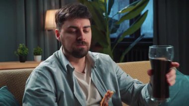 Abur cubur reklamı konsepti. Sakallı adam evde fast food dağıtımı ile vakit geçiriyor, kanepede oturup televizyon izliyor sosa batırılmış tavuk budu yiyor ve kola içiyor..