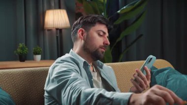 Abur cubur reklamı konsepti. Sakallı adam evde fast food dağıtımı ile vakit geçiriyor, kanepede oturup akıllı telefondan spor maçı izliyor ve cips yiyor, mutlu şarap cümleleri kuruyor..