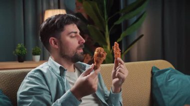 Abur cubur reklamı konsepti. Sakallı adam evde fast food teslimatlarıyla vakit geçiriyor, kanepede oturup televizyon seyrediyor, arkadaşının elini tutuyor, kokluyor ve ısırıyor, tadını çıkarıyor..