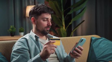 Abur cubur reklamı konsepti. Sakallı adam evde fast food dağıtımı ile vakit geçiriyor, kanepeye oturuyor, pirzola yiyor ve internetten alışveriş yapıyor, akıllı telefondan kart numarası yazıyor..