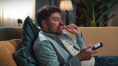 Abur cubur reklamı konsepti. Sakallı adam evde fast food dağıtımı ile zaman geçiriyor, kanepeye uzanıyor, televizyon izliyor ve kızarmış tavuk yiyor..