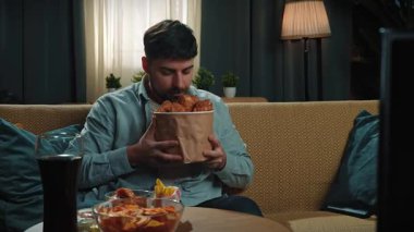 Abur cubur reklamı konsepti. Sakallı adam evde fast food teslimatlarıyla vakit geçiriyor, kanepede oturup televizyon izliyor, kova ve sos bölümünden kızarmış tavuk bacağı alıyor. Yavaş çekim