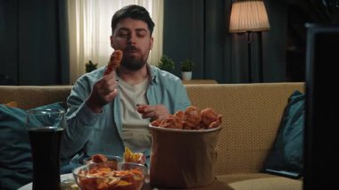 Abur cubur reklamı konsepti. Sakallı adam evde fast food teslimatlarıyla vakit geçiriyor, kanepede oturup televizyon izliyor, kızarmış tavuk budu sosuna batırıyor ve tadını çıkarıyor. Yavaş çekim