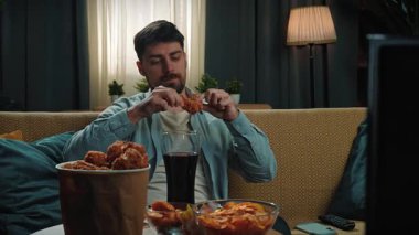 Abur cubur reklamı konsepti. Sakallı adam evde fast food teslimatlarıyla vakit geçiriyor, kanepede oturup televizyon izliyor, kızarmış tavuk budu sosuna batırıyor ve tadını çıkarıyor. Yavaş çekim